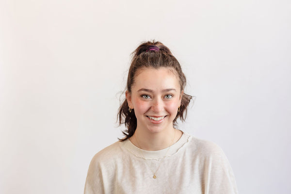 Woman with a ponytail wearing a beige sweater against a white background